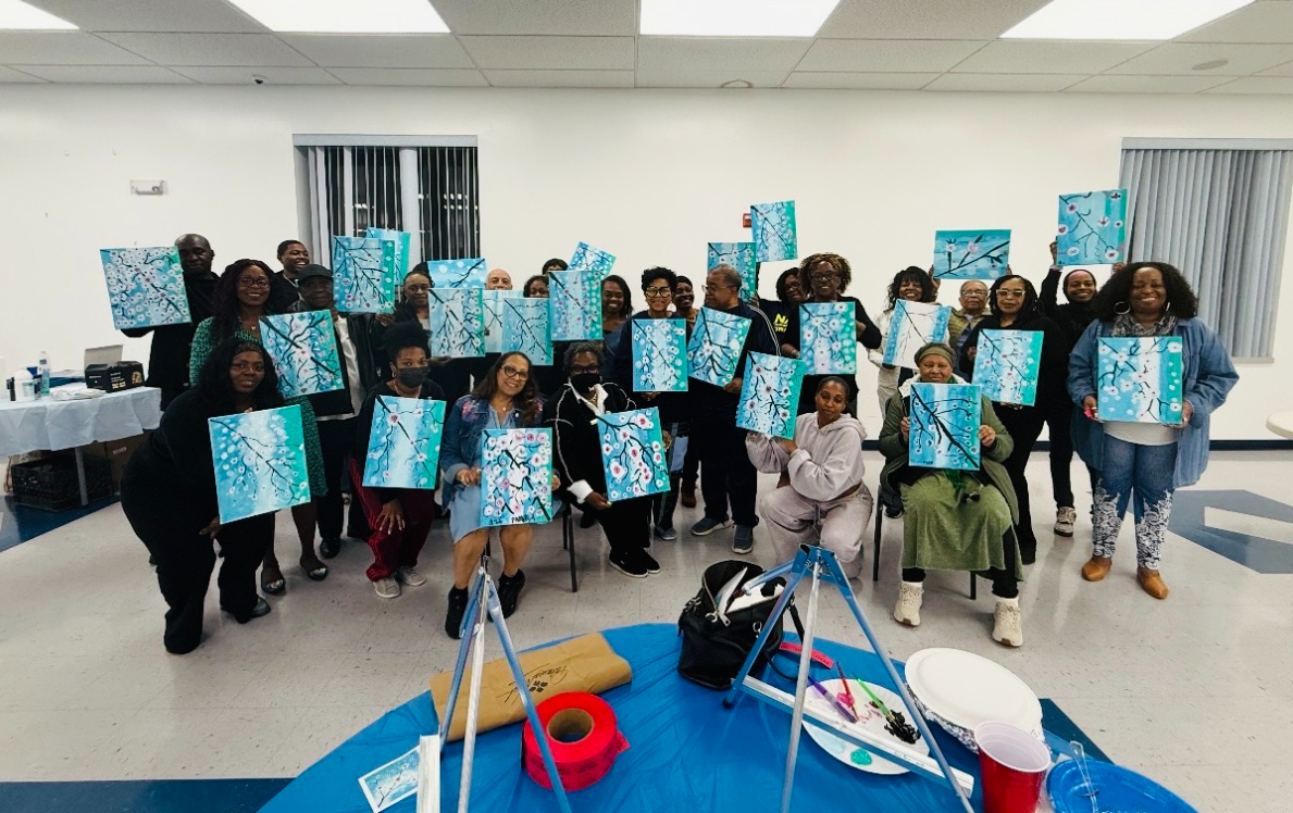 Group of guests proudly showing their finished cherry-blossom paintings at a paint party